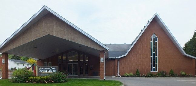 Centennial Park Baptist Church, a red-brick church with a steep A-frame gable and a tall narrow window, beside a wide gabled canopy over the entrance and the church sign