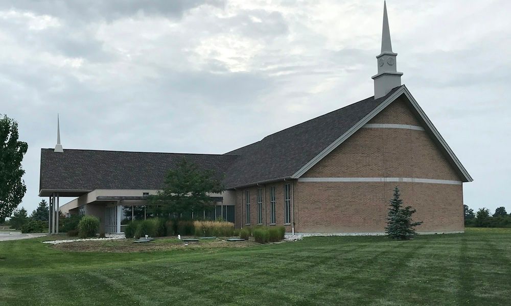 Covenant Canadian Reformed Church, a long brick church with a pale band across its gable, a white steeple and a covered entrance, behind a wide lawn