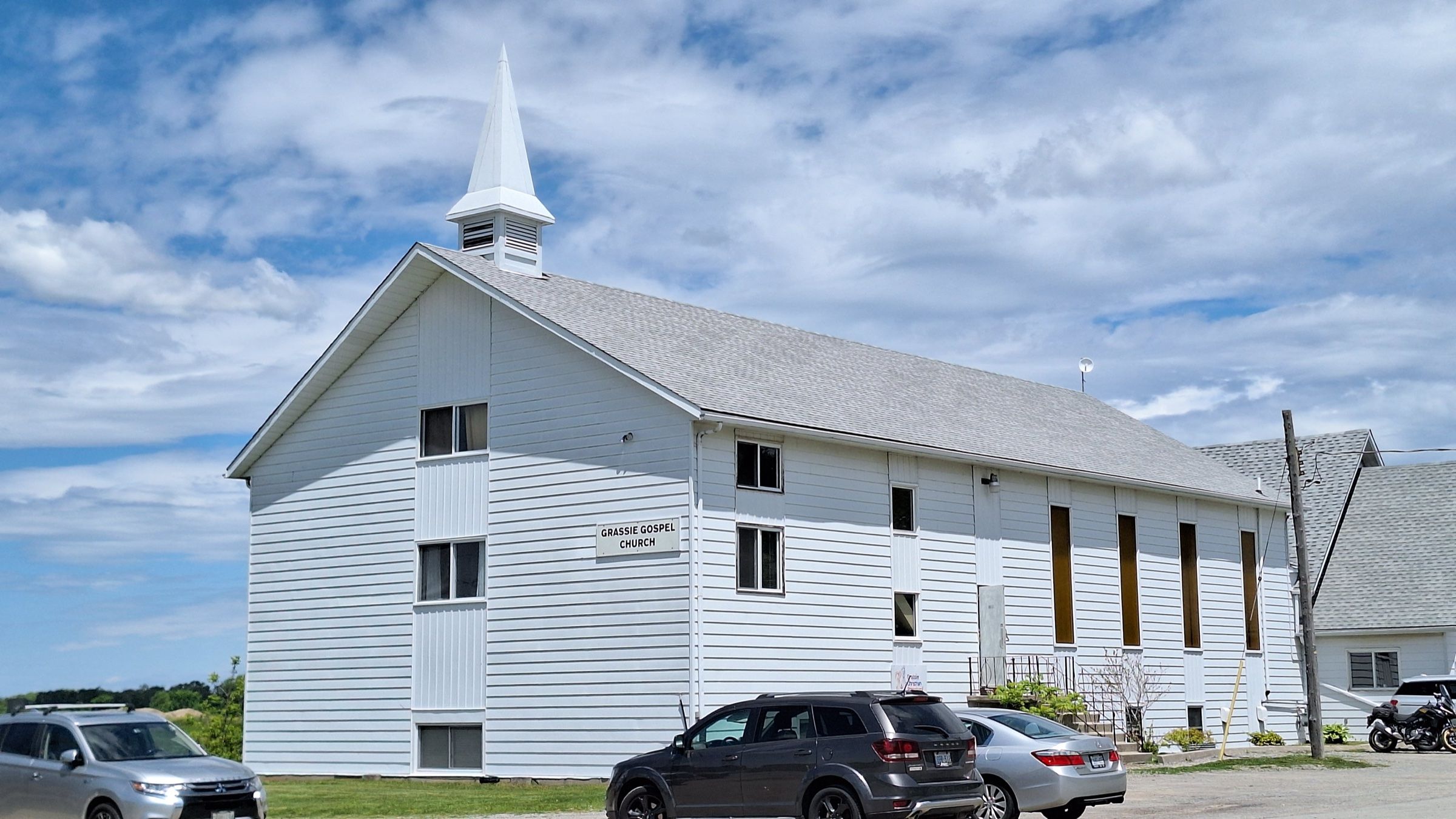 The white clapboard church on Mud Street West where Grace Community Church meets, with a white steeple at its gable end and a sign on its side still reading Grassie Gospel Church