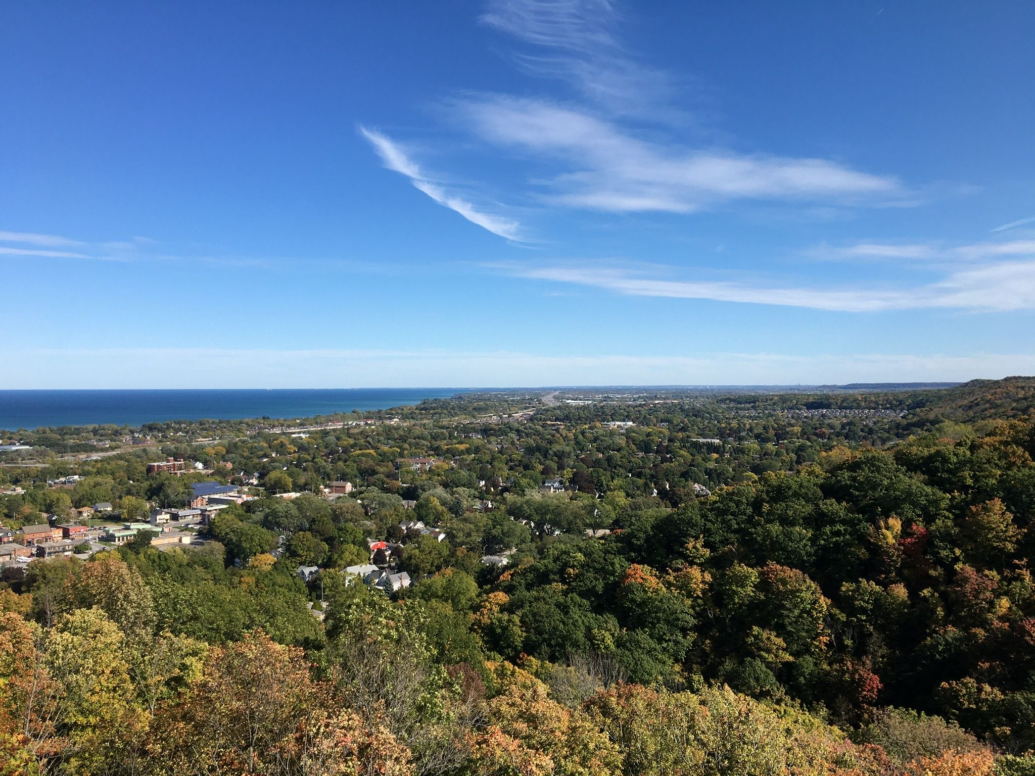 Grimsby seen from the Niagara Escarpment in autumn, the town's roofs among turning trees and Lake Ontario beyond